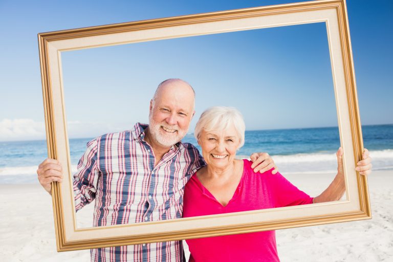 Senior,Couple,Holding,Frame,At,The,Beach