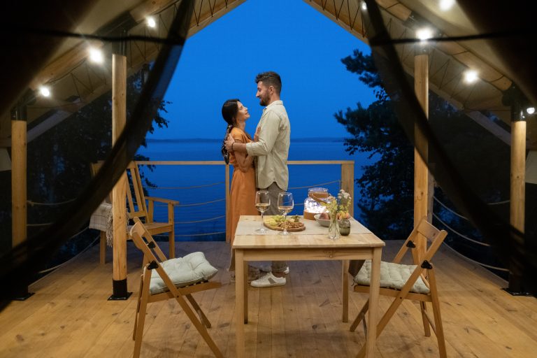 Young,Couple,Standing,In,Embrace,On,Terrace,Of,Glamping,House