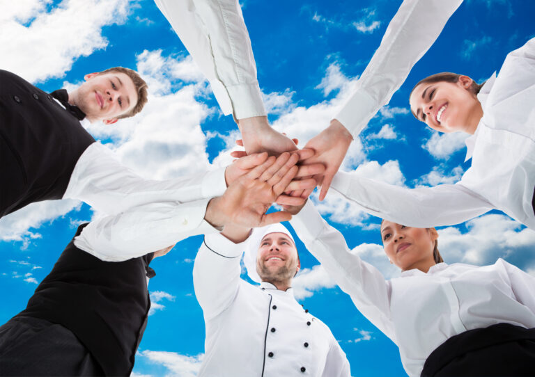 Low,Angle,View,Of,Waiters,And,Waitresses,Stacking,Hands,Against